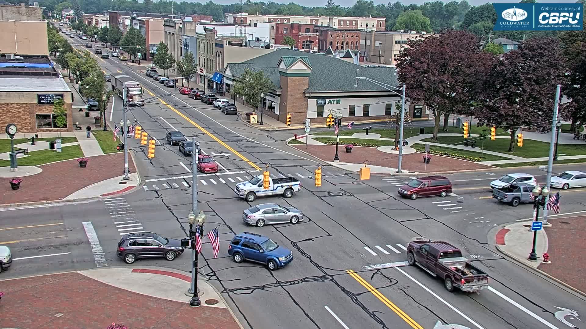 A high-angle view of a town's intersection with several vehicles, under a partly sunny sky.