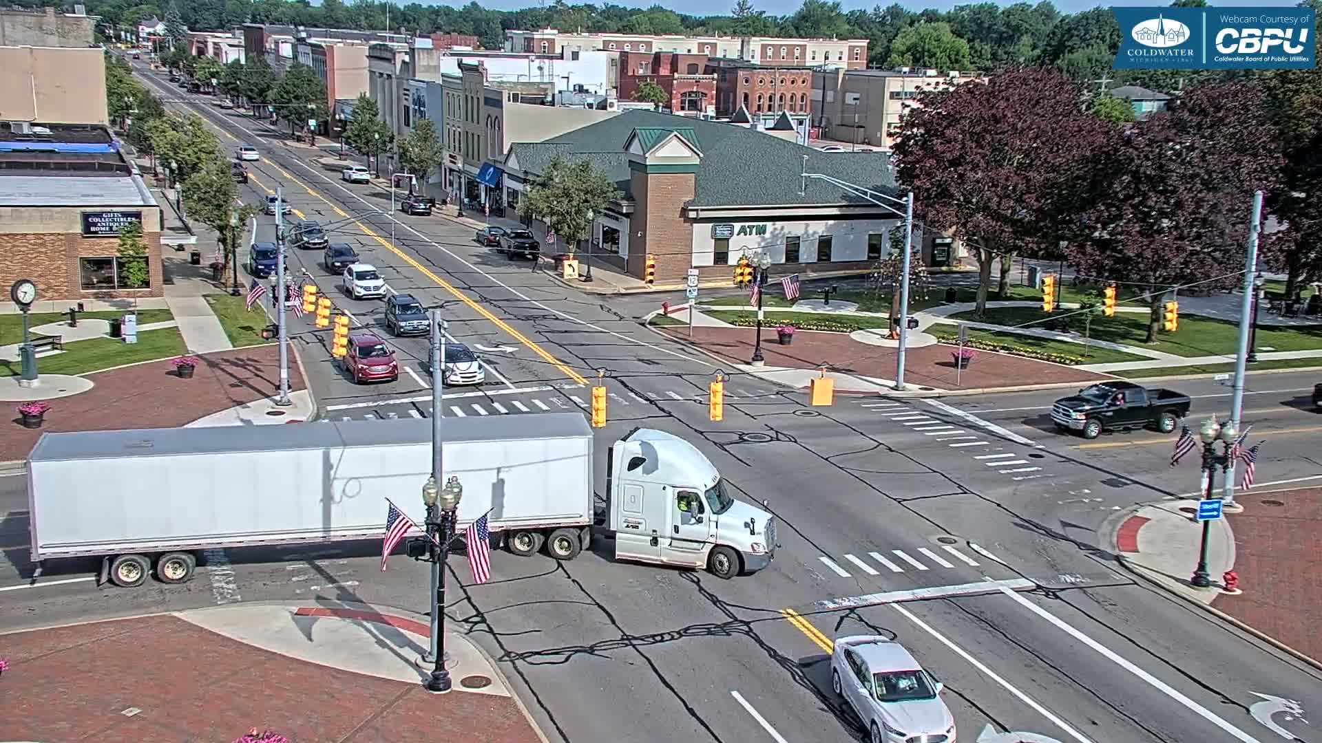 A semi-truck and several cars are navigating a city intersection on a sunny day.