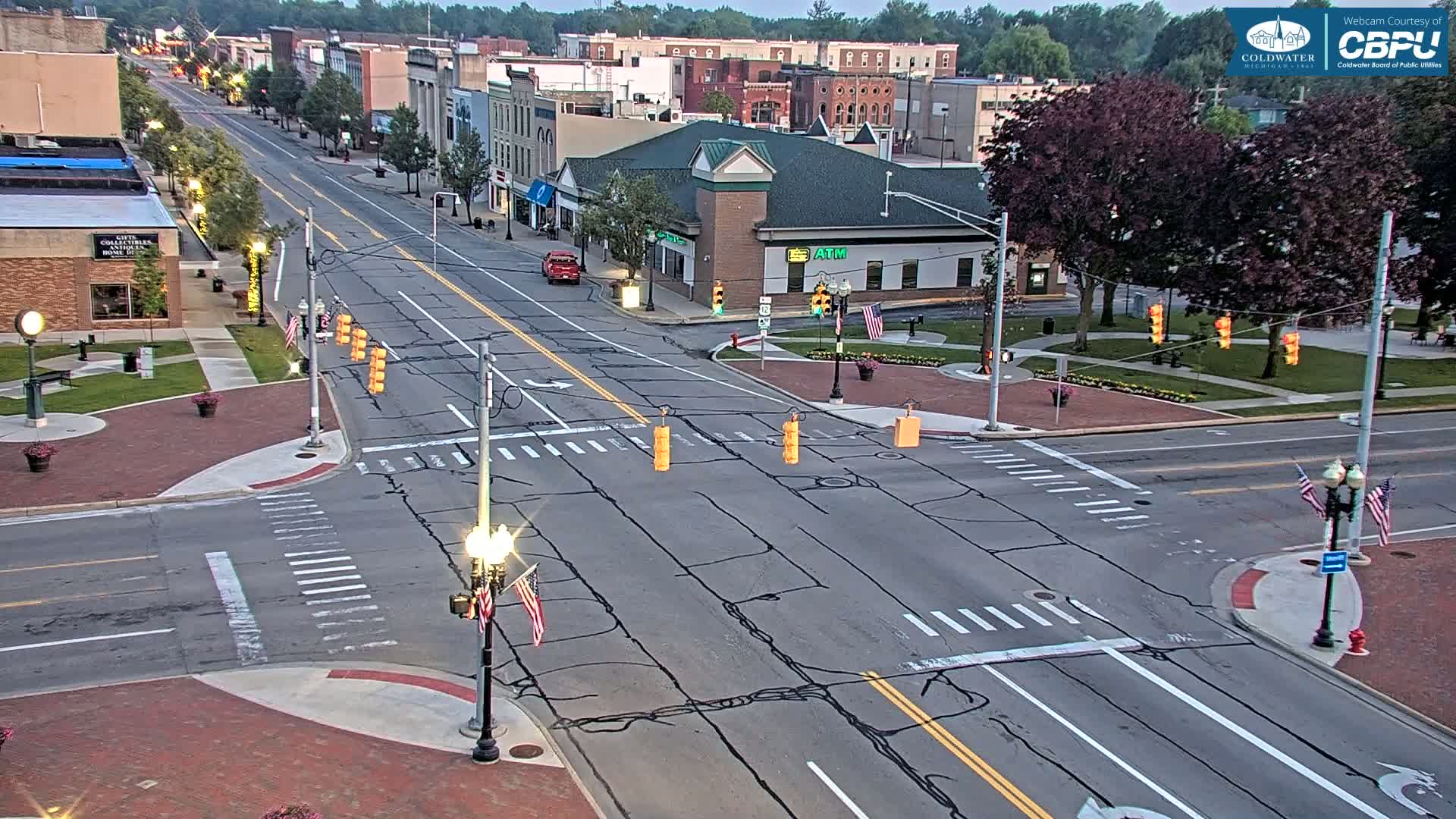 A mostly empty street intersection in a town, with several buildings visible in the background under a partly cloudy sky.