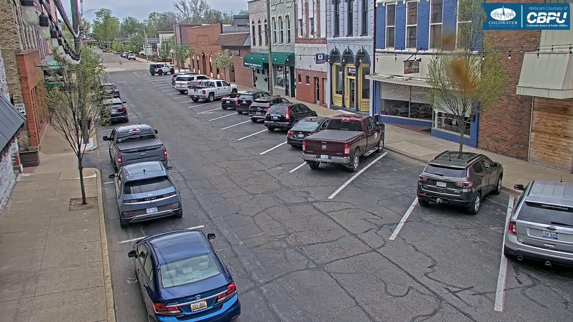 Cars are parked along a street in front of brick buildings on an overcast day.