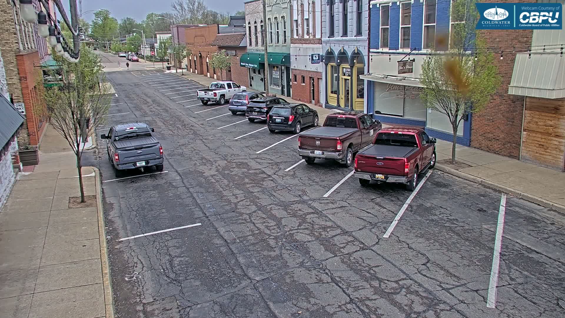 Several trucks and cars are parked along a cracked asphalt street in front of brick buildings on an overcast day.