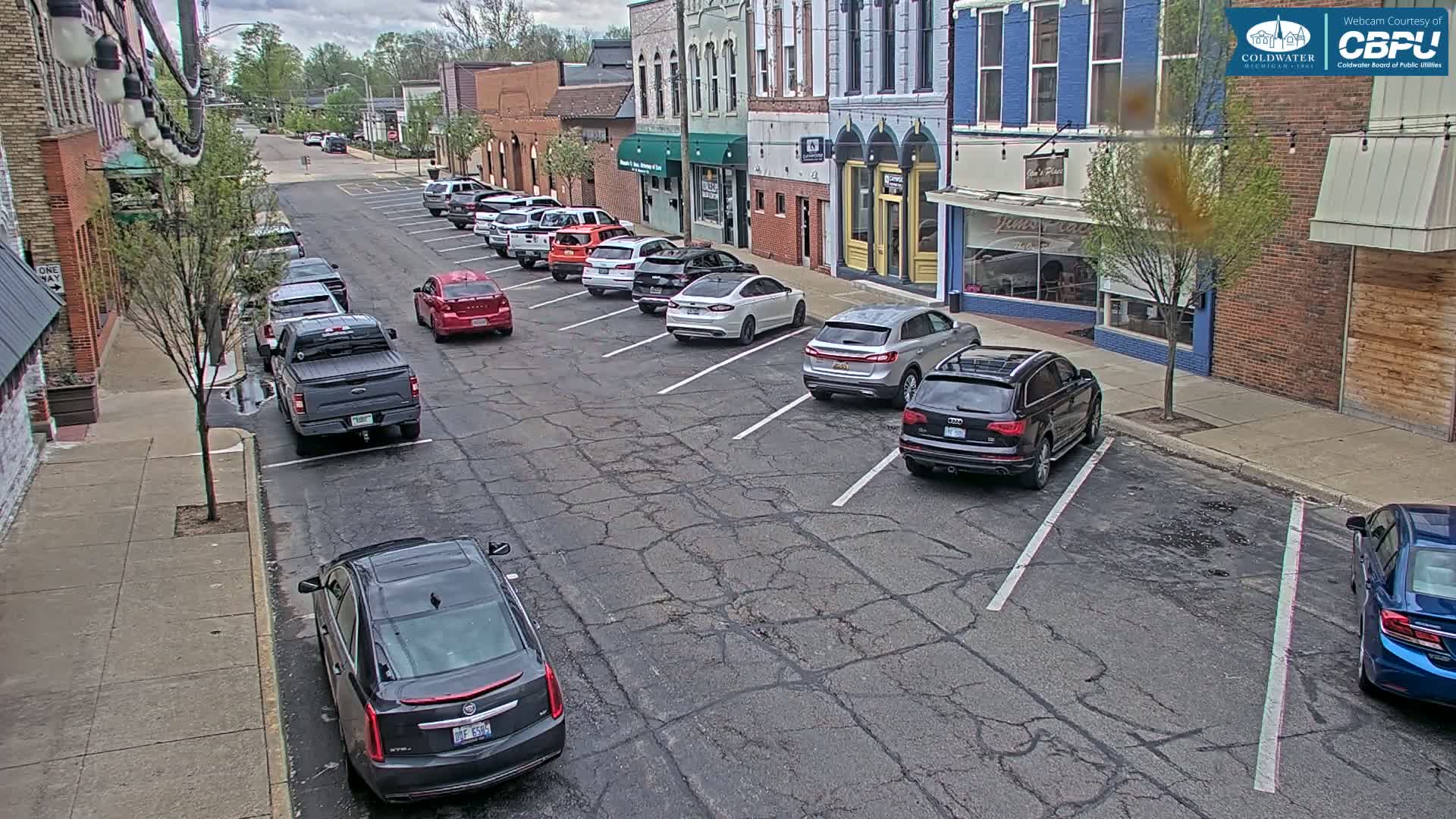 A street lined with parked cars in front of brick buildings on a partly cloudy day.