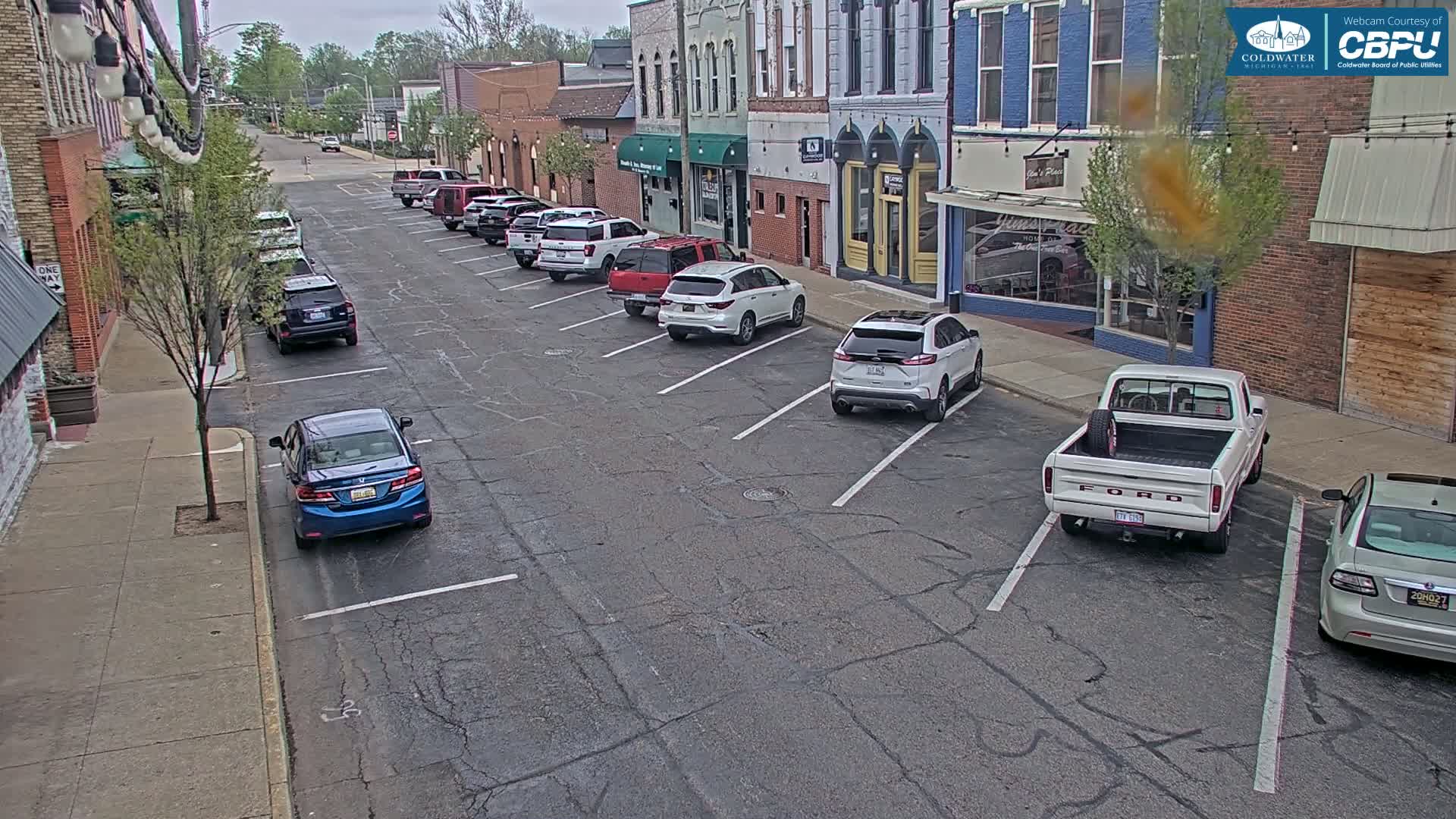 A street with parked cars lines both sides, under an overcast sky.