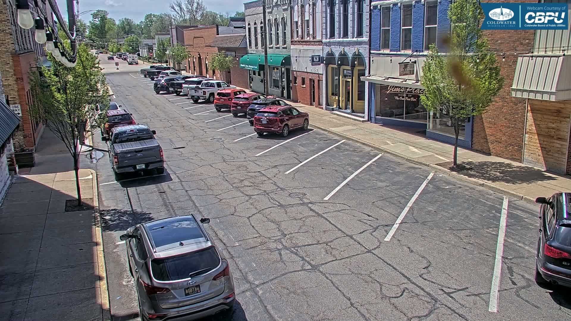 Several cars are parked along a sunny street in front of brick buildings.