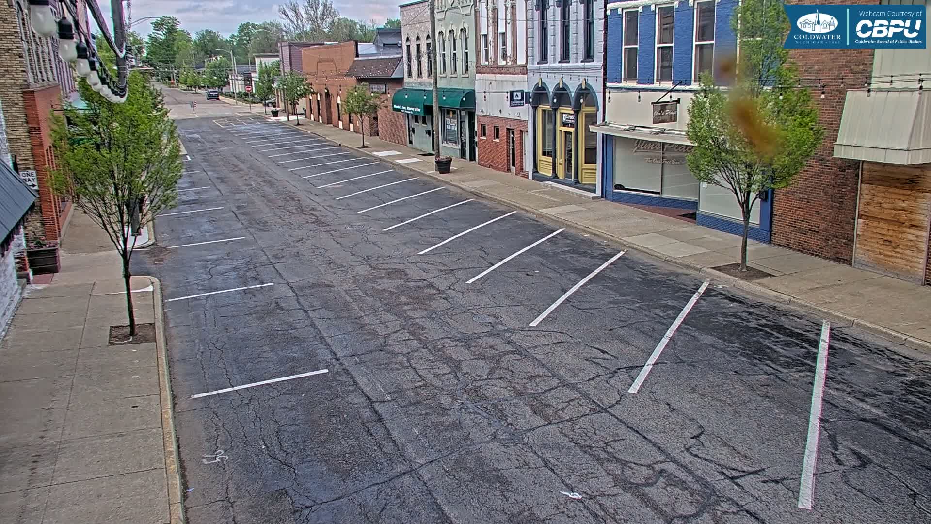 A mostly empty street with parallel parking spaces lines a row of brick buildings on a partly cloudy day.