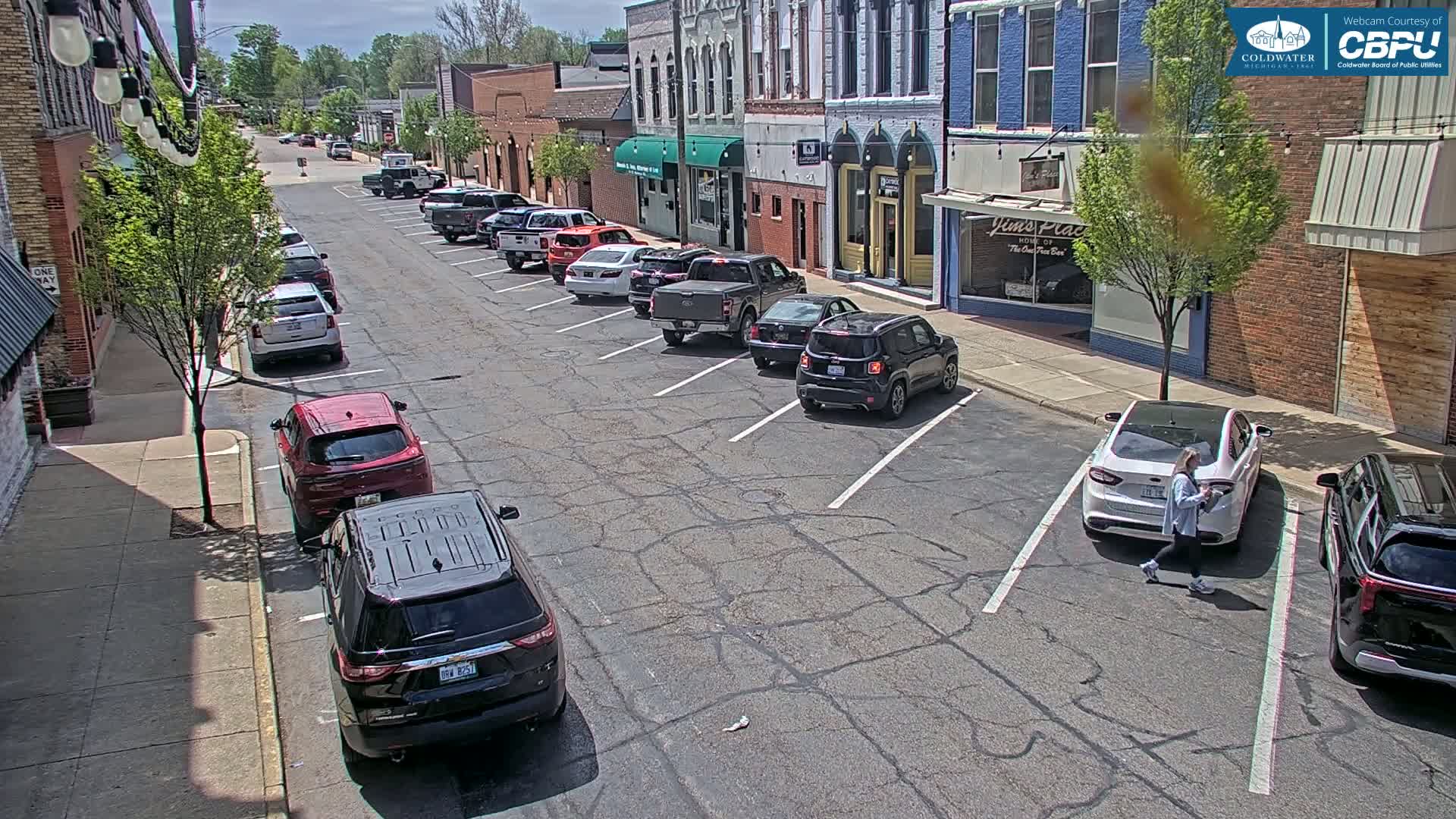 Cars are parked along the street in front of brick buildings on a sunny day.