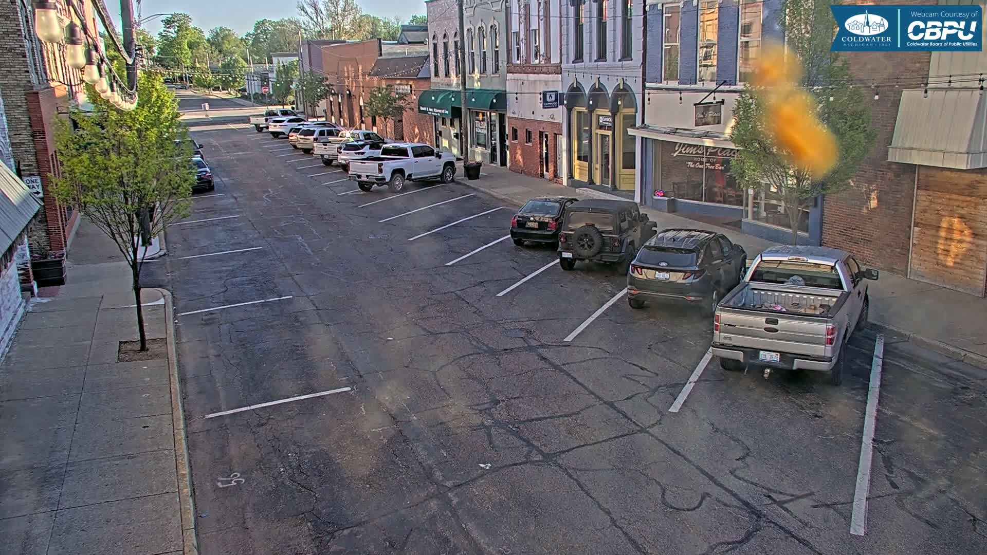 Cars are parked along a street in front of brick buildings on a sunny day.