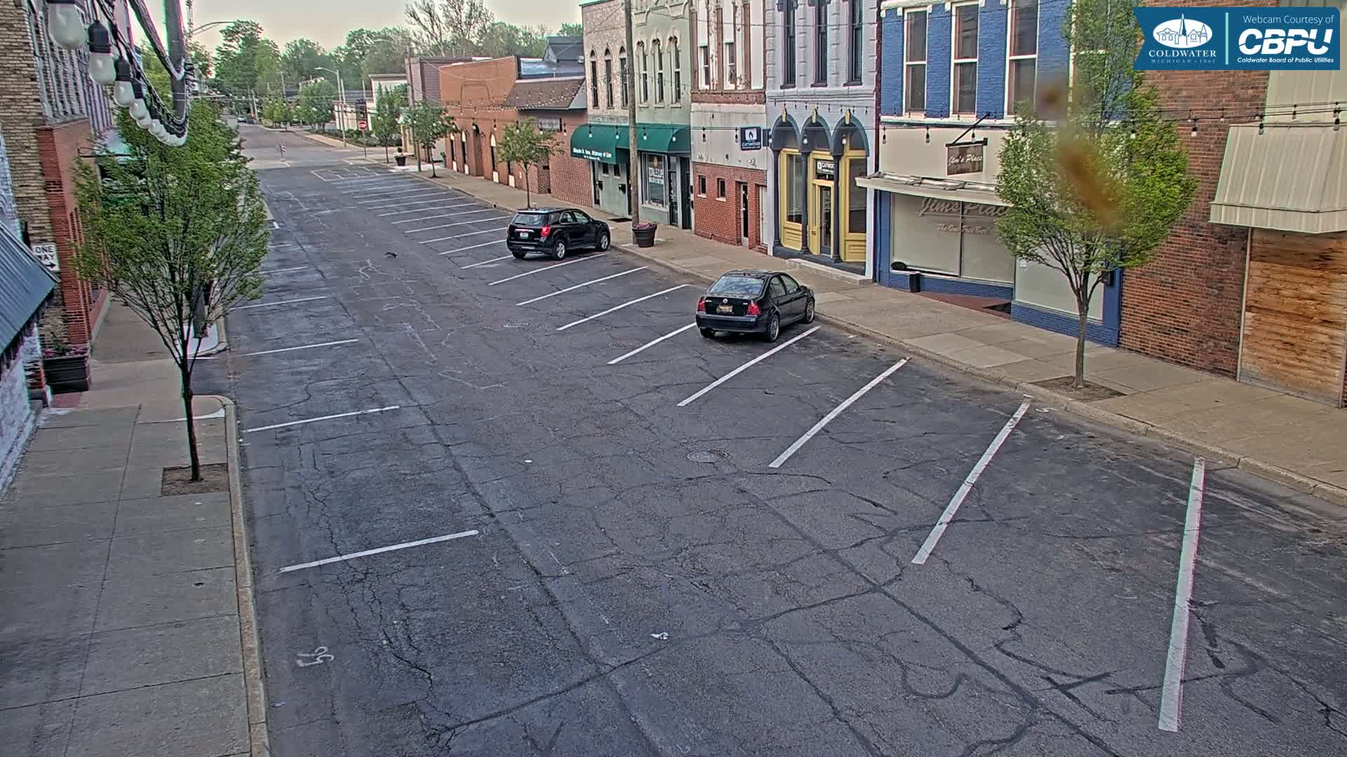 A mostly empty street with parked cars in front of brick buildings on an overcast day.