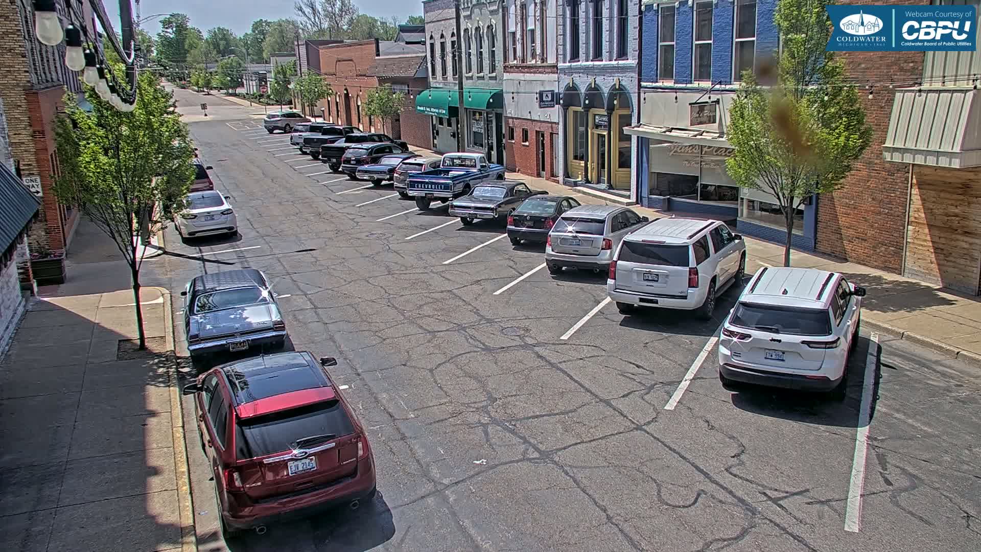 A sunny street lined with parked cars in front of brick buildings.