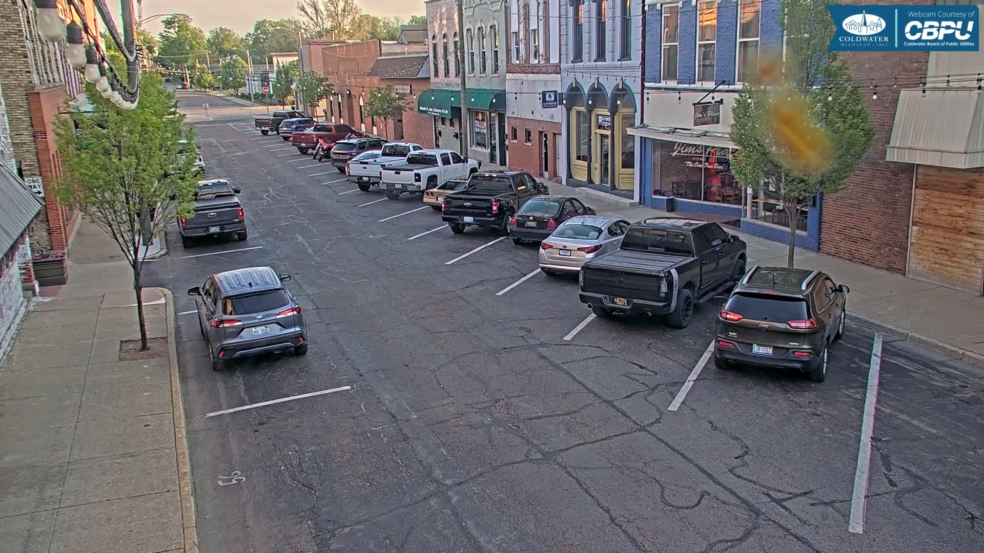 A street with parked cars lines both sides, under a partly sunny sky.