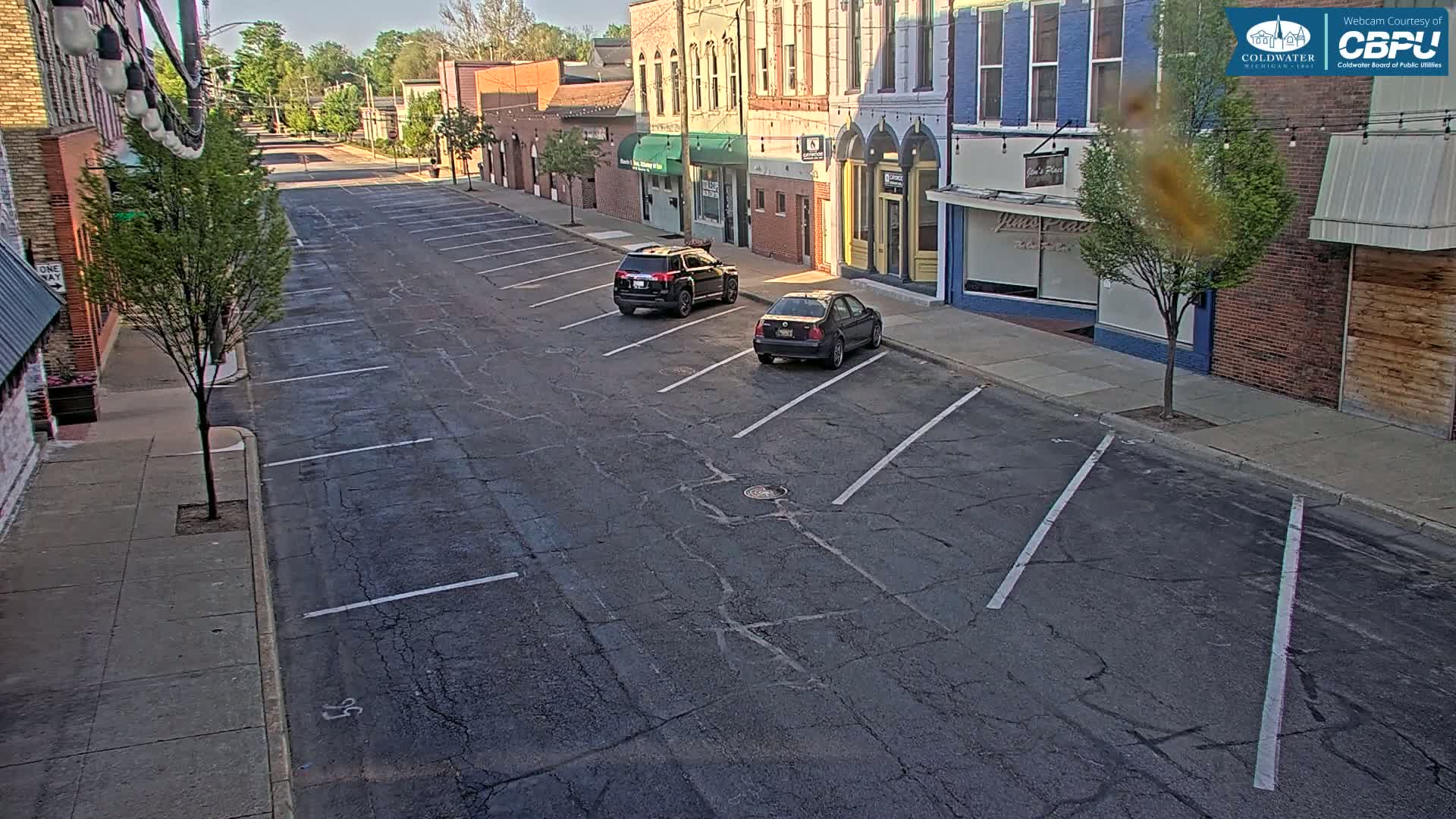 A mostly empty street with parked cars lines a row of buildings on a sunny day.