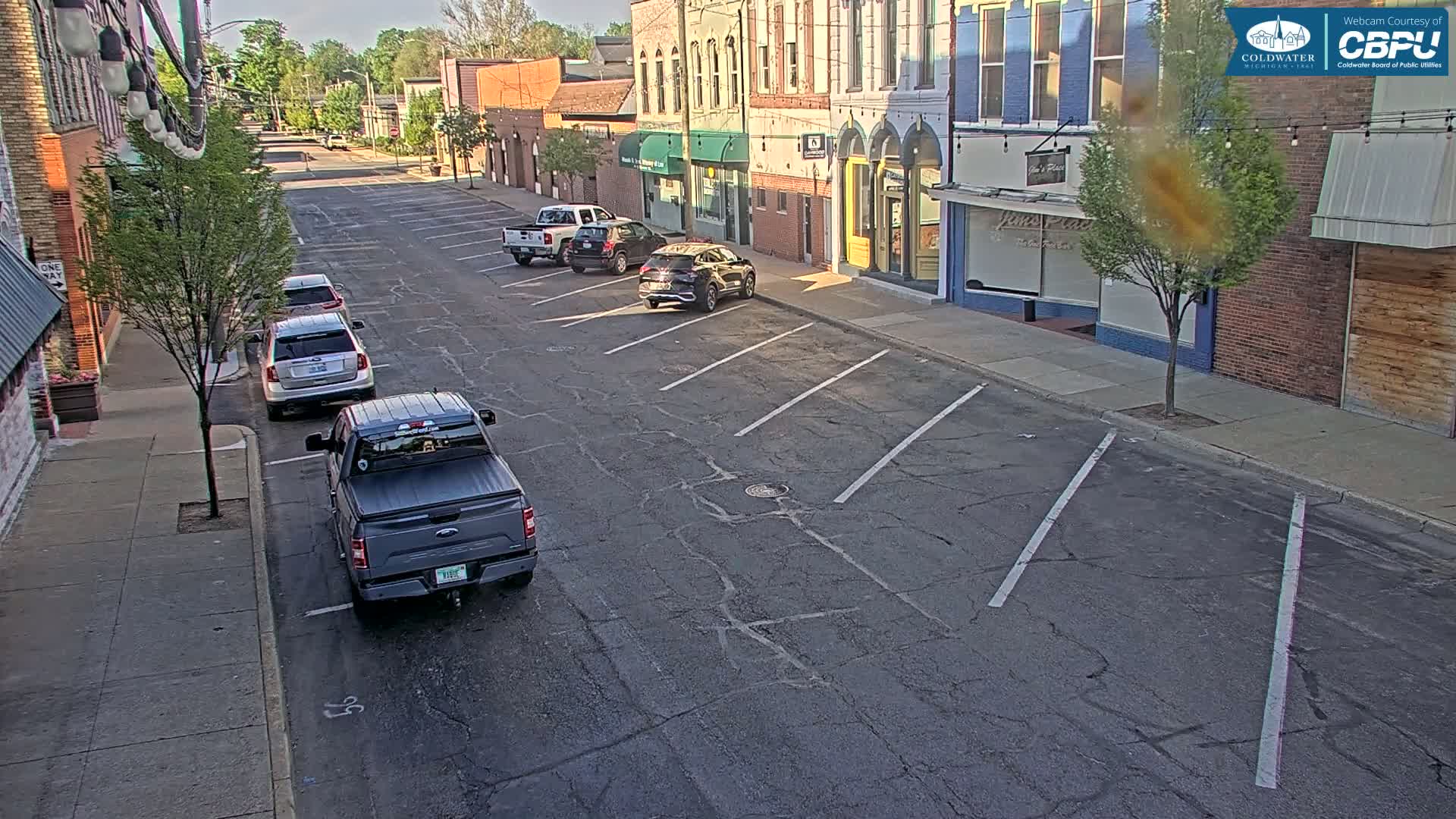 Several cars are parked along a street in front of brick buildings on a sunny day.