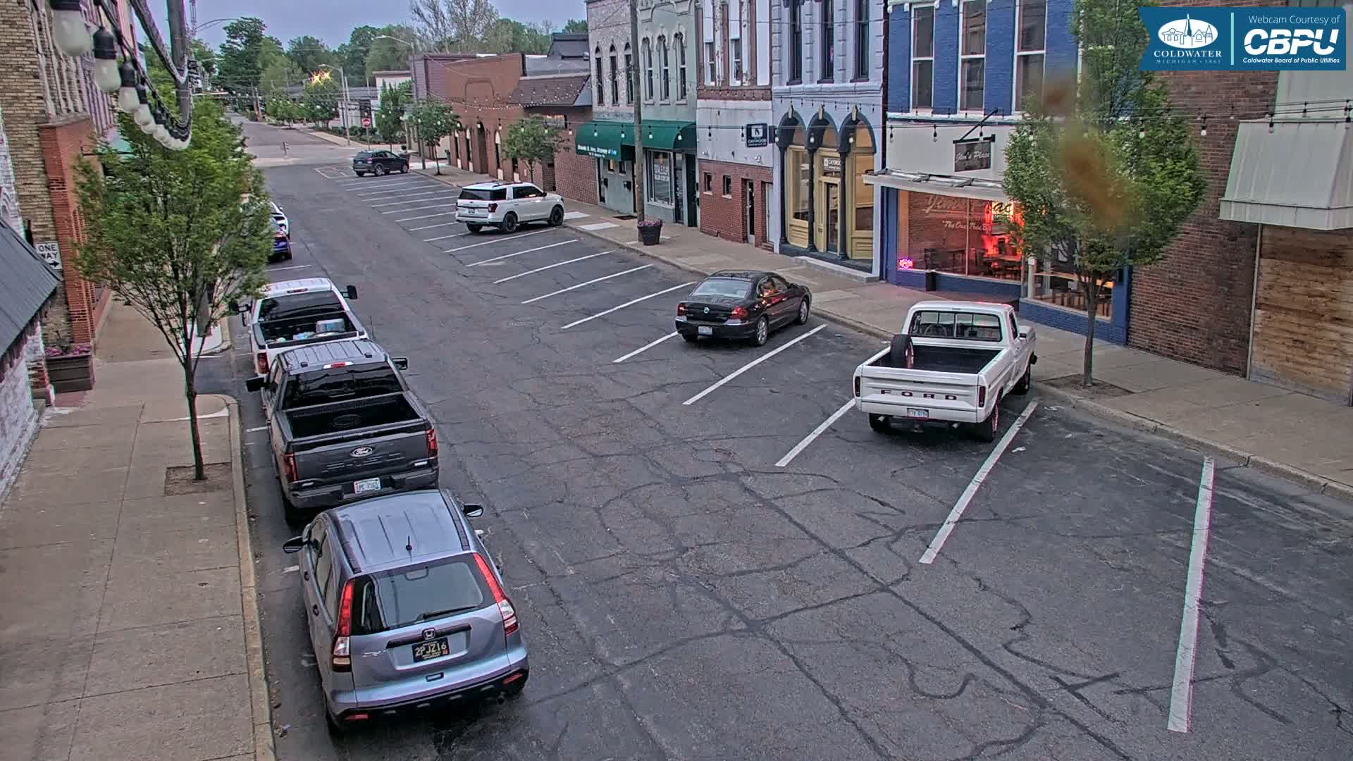 A mostly empty street lined with parked cars and brick buildings under an overcast sky.