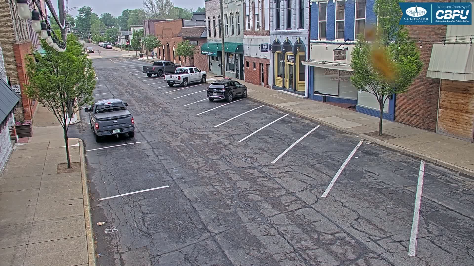 A mostly empty street with parked cars lines brick buildings on an overcast day.