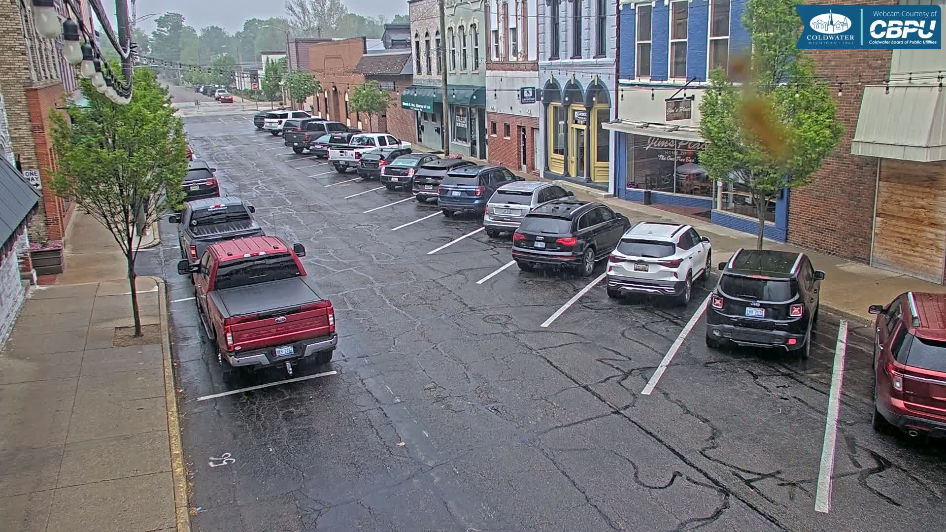 A rain-slicked street lined with parked cars in front of brick buildings.