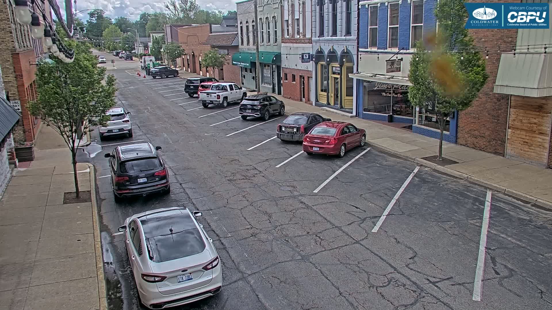 A street lined with parked cars and brick buildings under a partly cloudy sky.