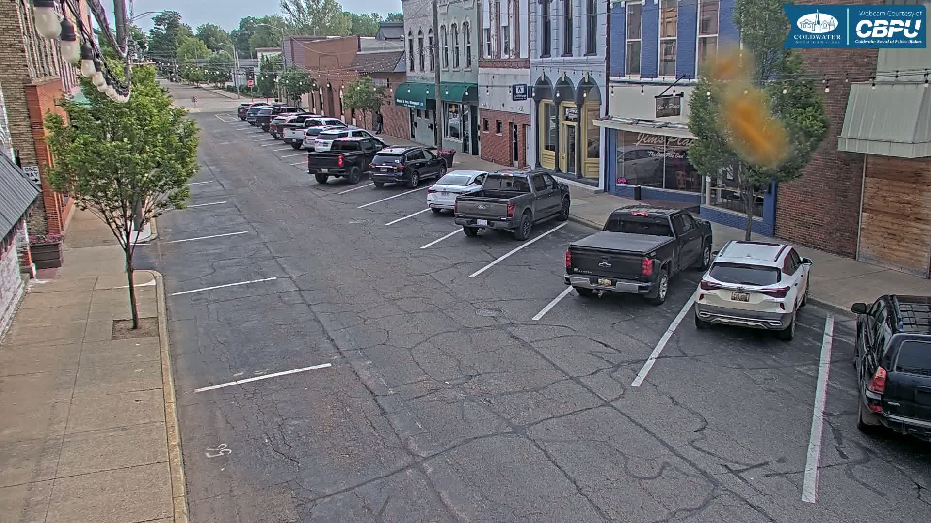 Cars are parked along a street in front of brick buildings on an overcast day.