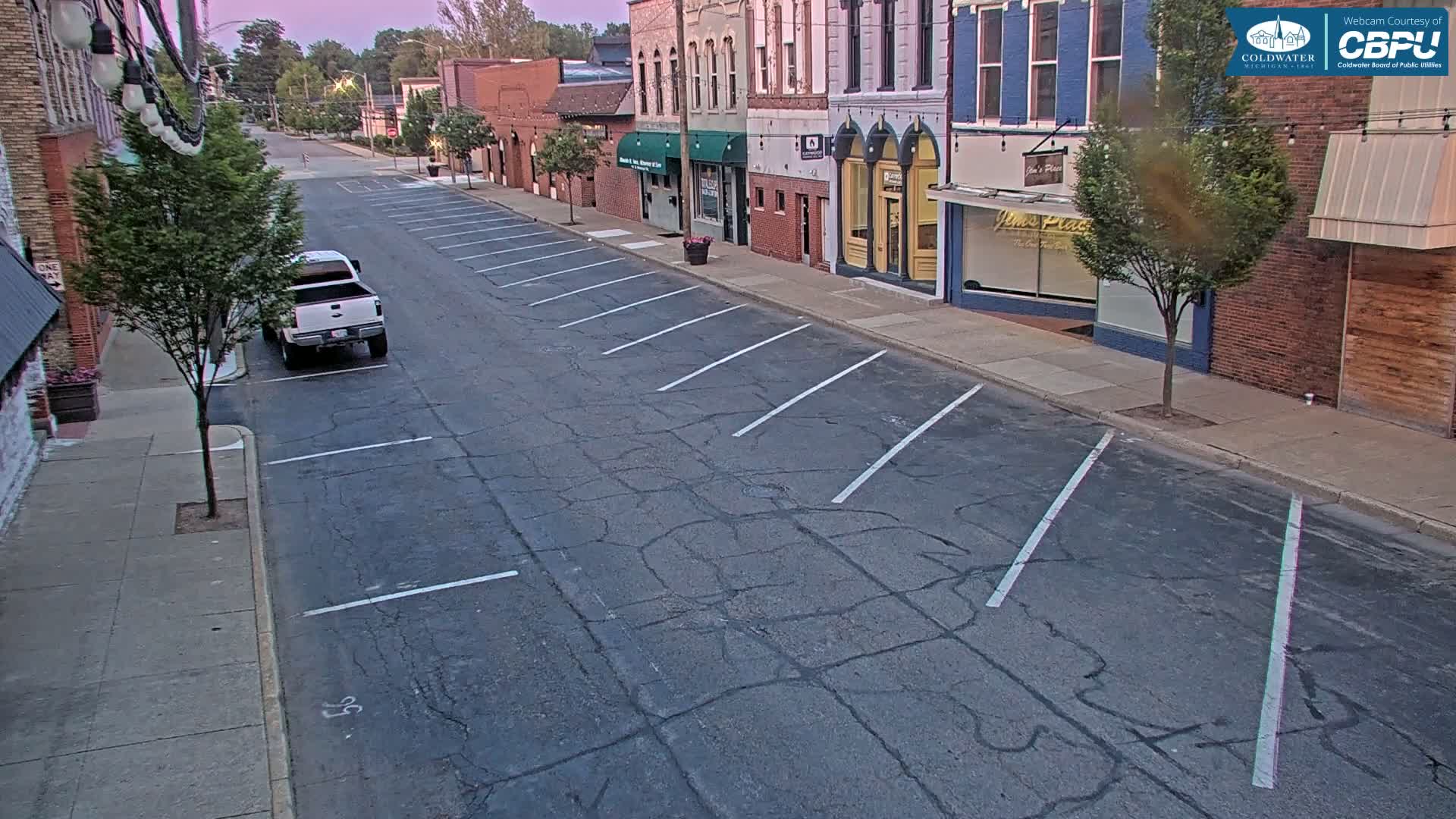 A mostly empty street with parking spaces on the side, lined with brick buildings under a twilight sky.