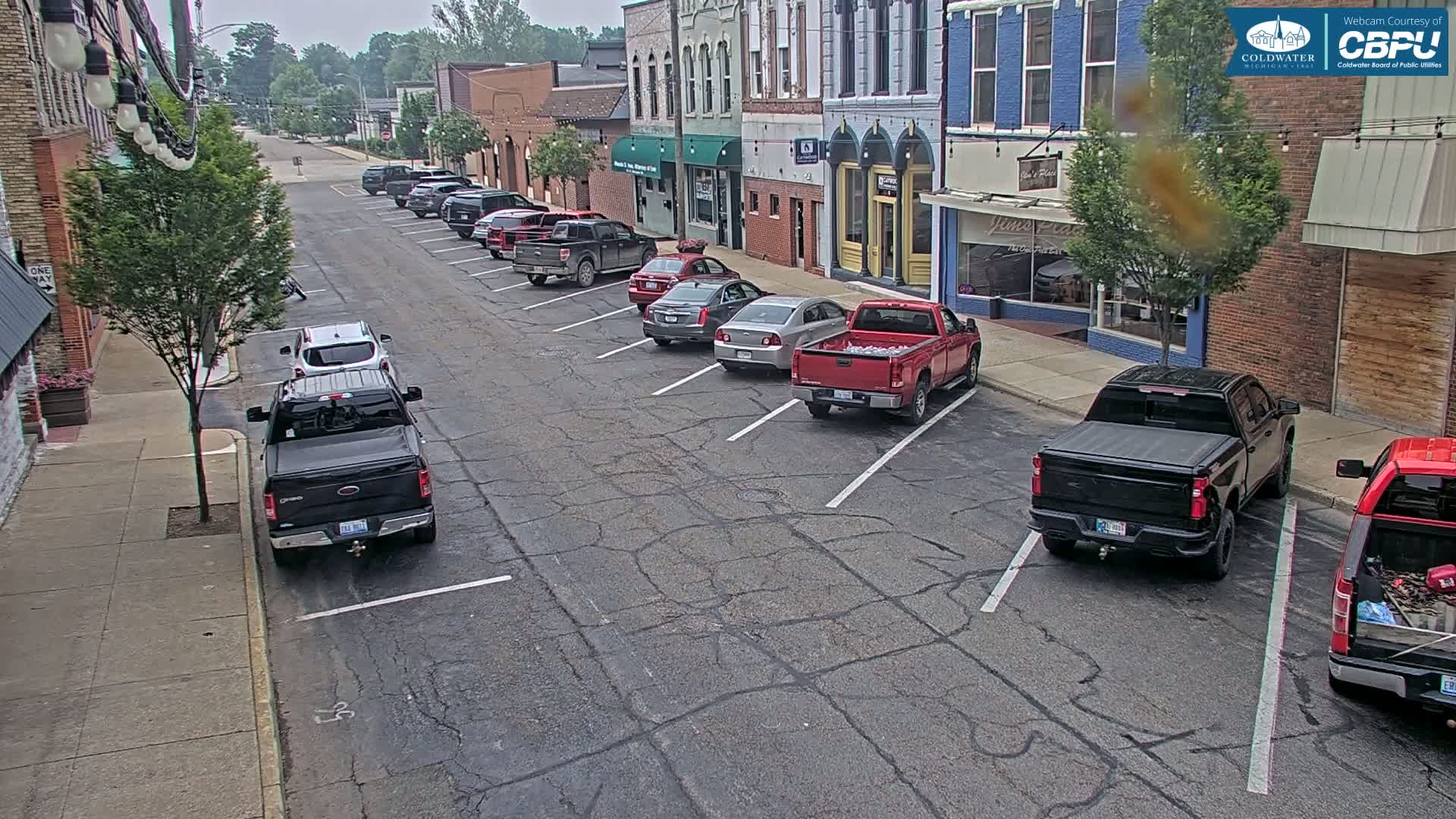 Several vehicles are parked along a street in front of brick buildings on an overcast day.