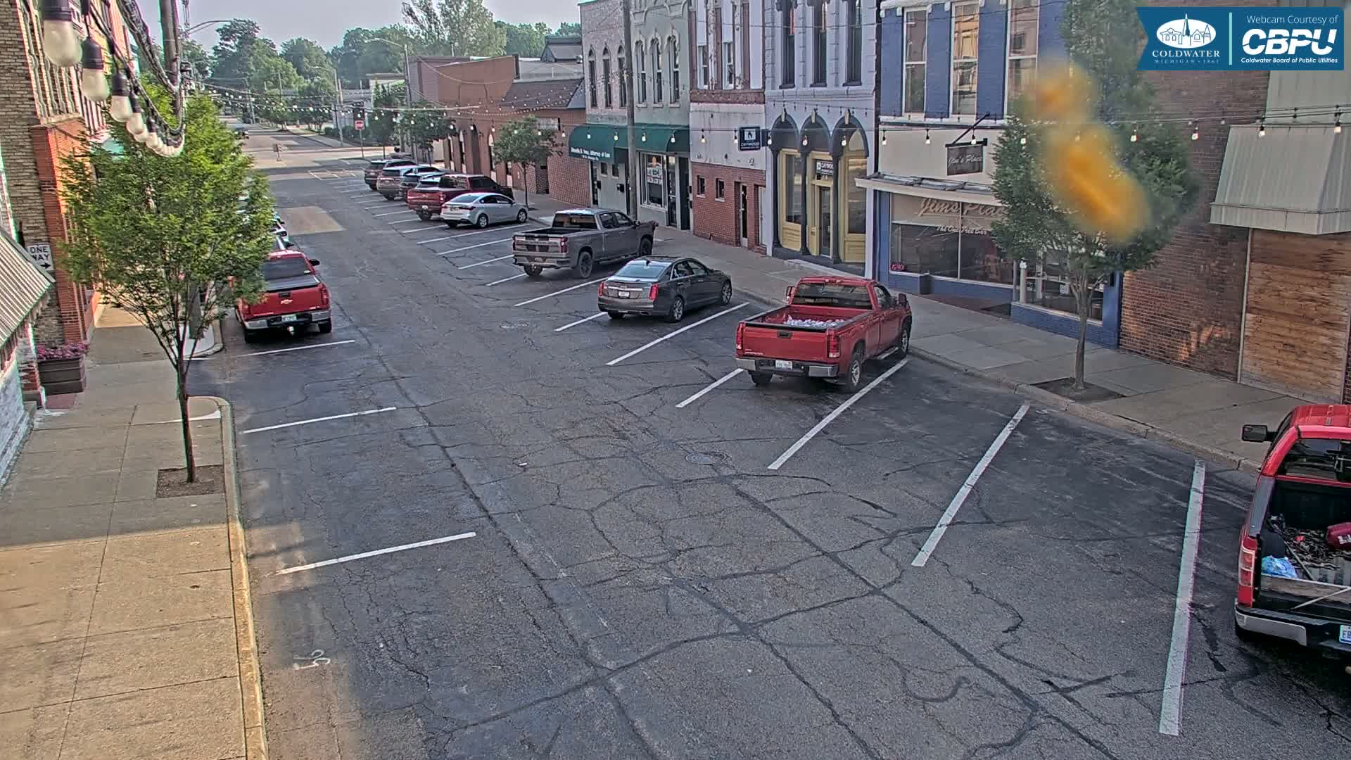 Several cars are parked along a street lined with brick buildings on a sunny day.