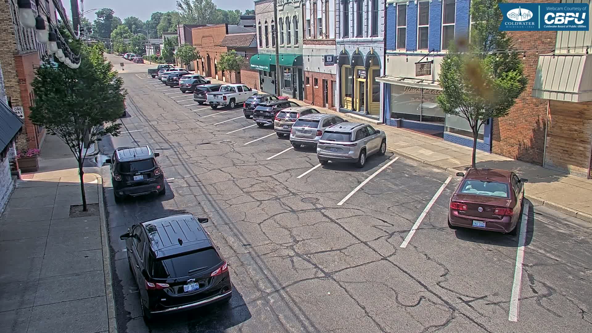 Several cars are parked along a street lined with brick buildings on a sunny day.