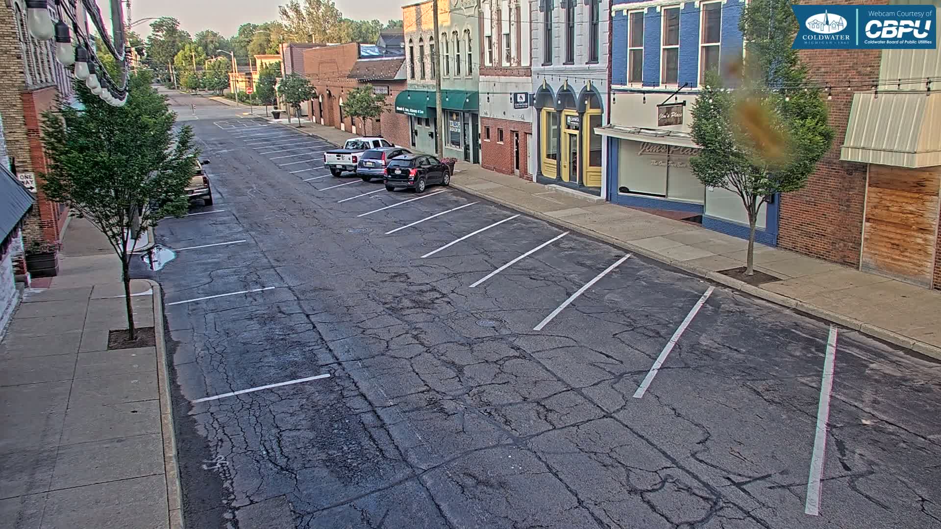 A mostly empty street with parked cars in front of brick buildings on a sunny day.
