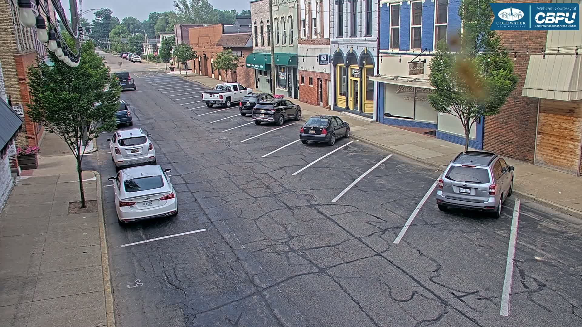 Several cars are parked along a street lined with brick buildings on a partly cloudy day.