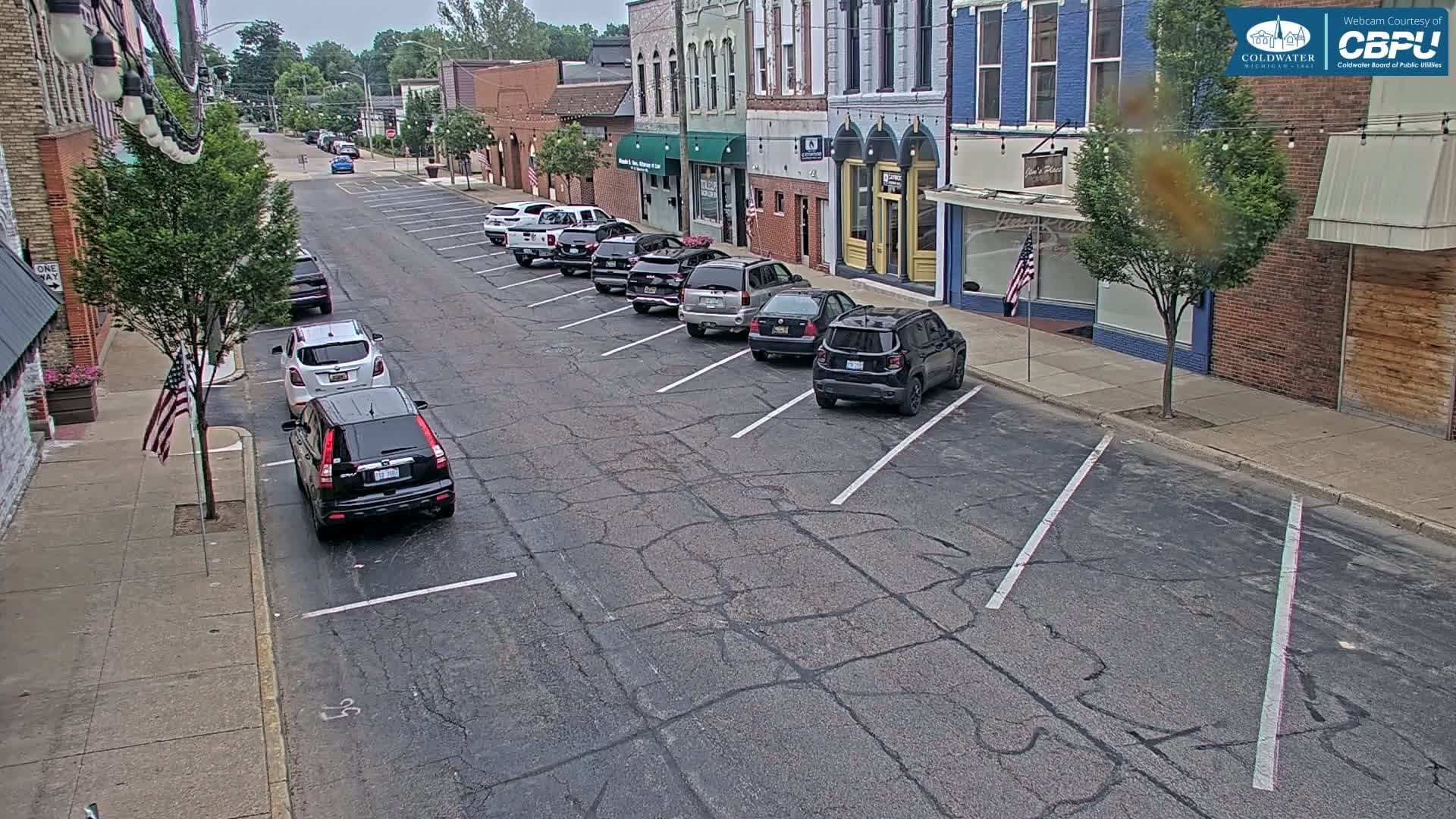 A street scene on an overcast day shows several cars parked along the side of a street in front of brick buildings.