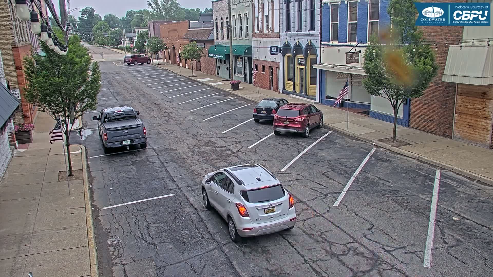 A mostly empty street lined with brick buildings on an overcast day, containing several parked cars and a pickup truck.