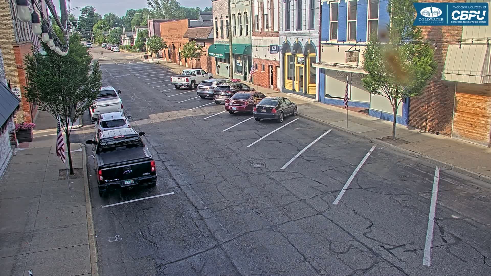 Several cars are parked along a street in front of brick buildings on a sunny day.