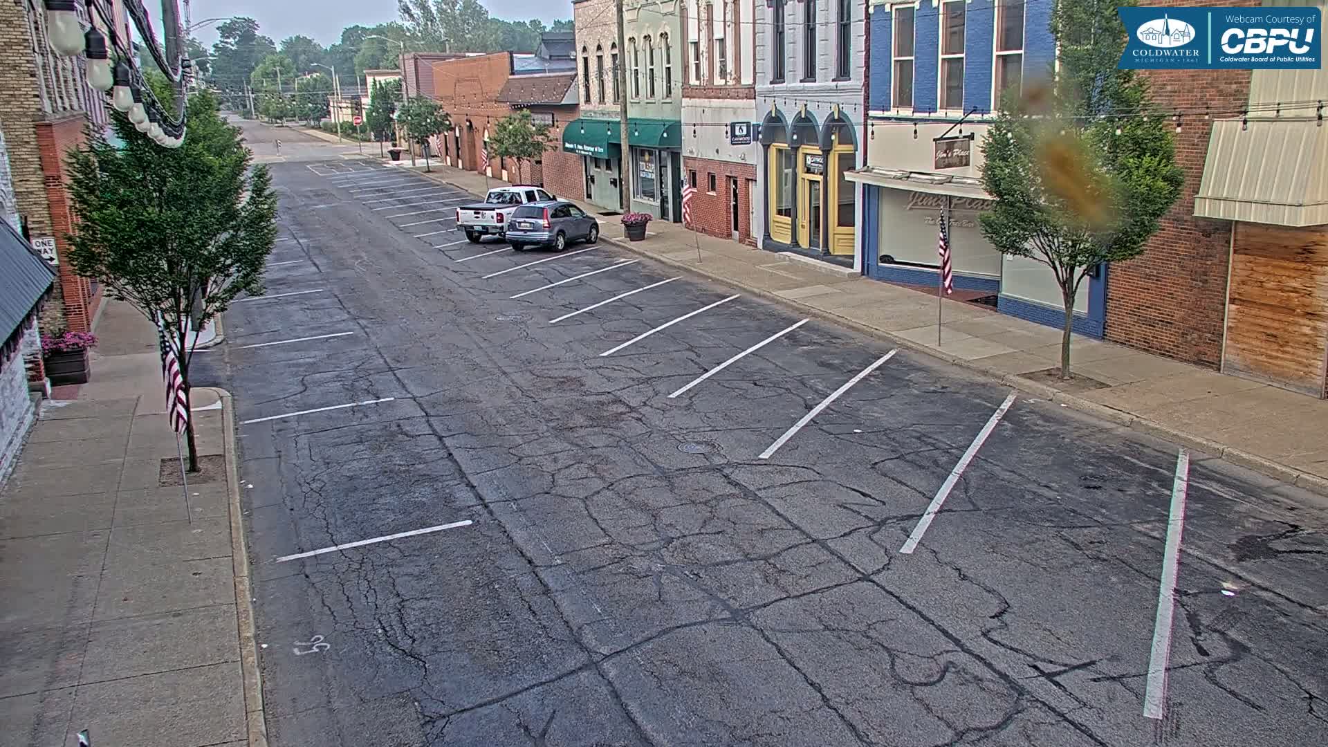 A mostly empty street lined with two-story buildings on an overcast day, with a few cars parked along the side.