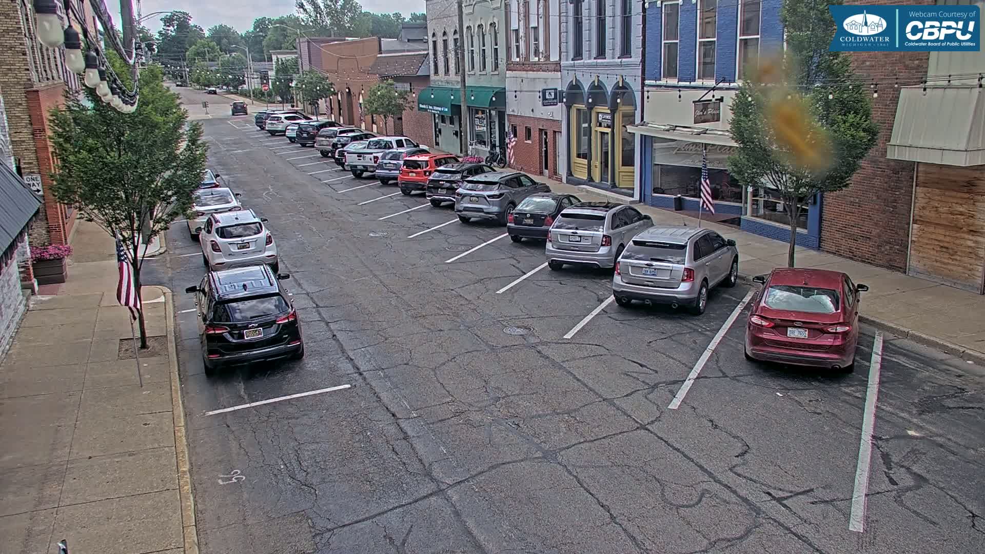 Cars are parked along a street in front of brick buildings on an overcast day.