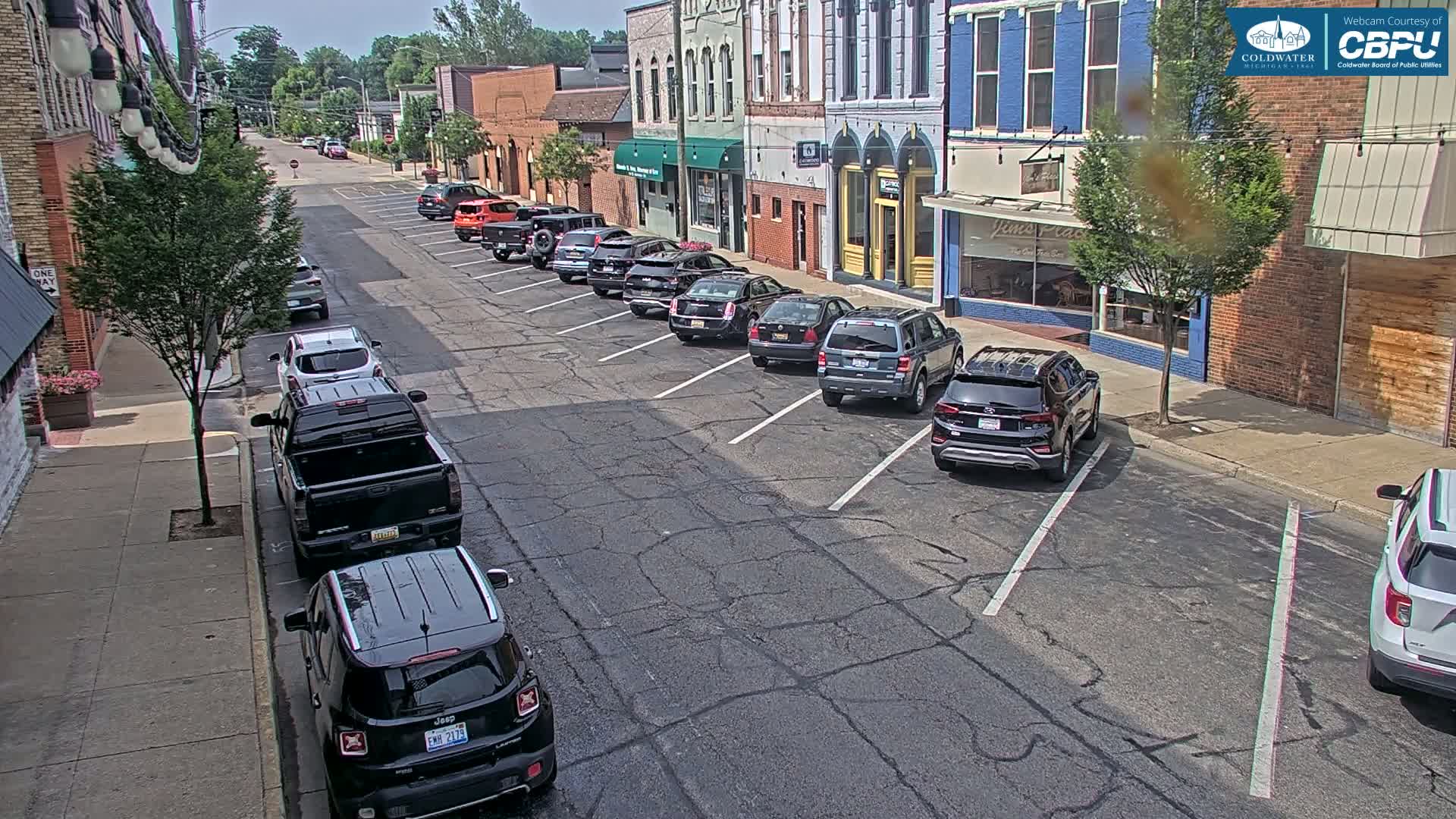 A sunny day on a street lined with parked cars in front of brick buildings.