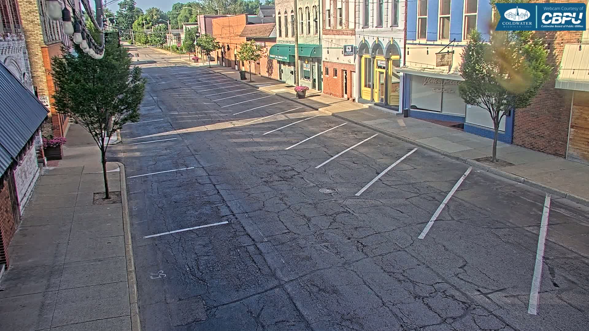 A mostly empty street with parallel parking spaces on a sunny day in front of several brick buildings.