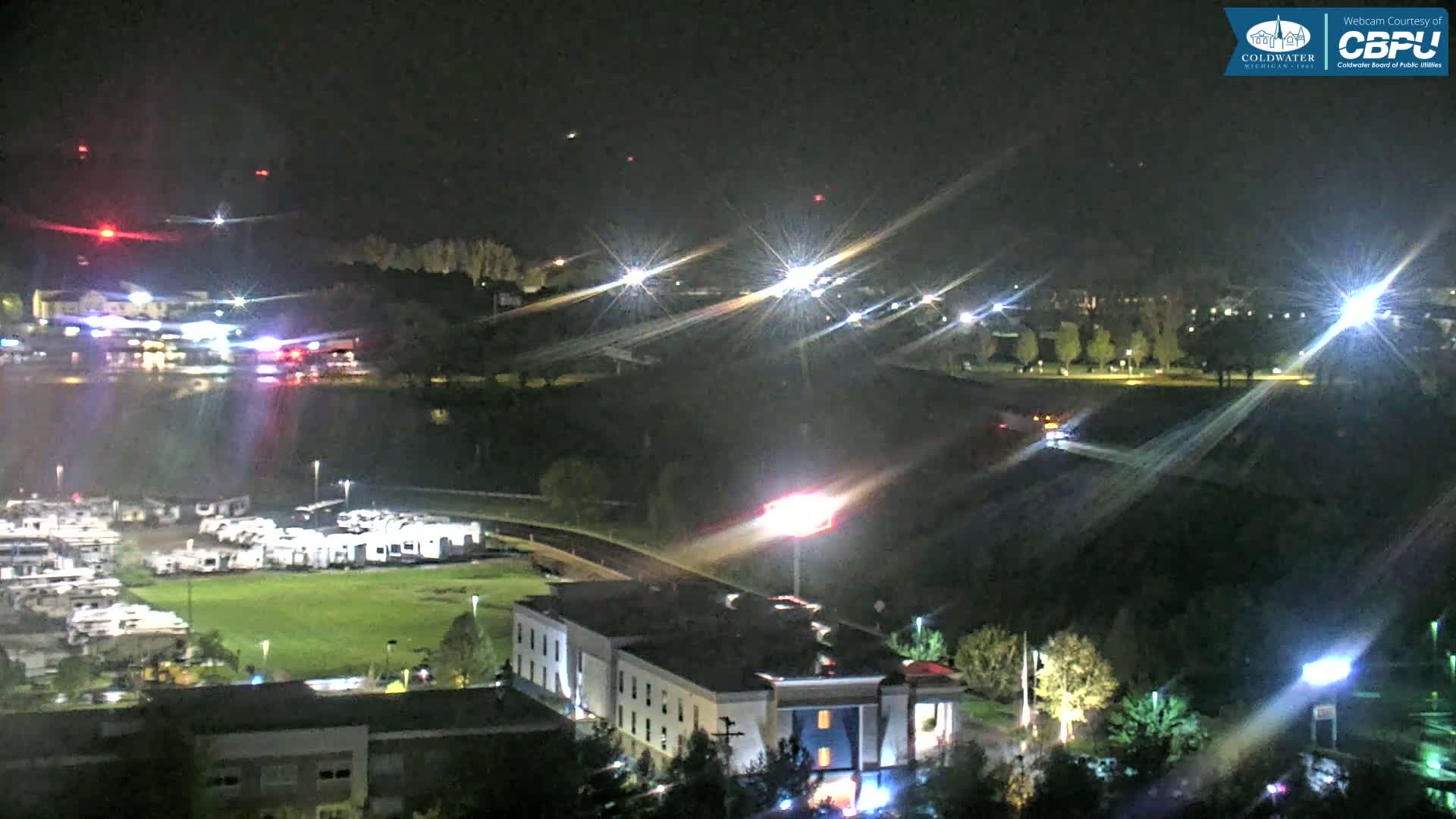 A nighttime aerial view shows a hotel, RV park, and surrounding landscape illuminated by artificial lights.