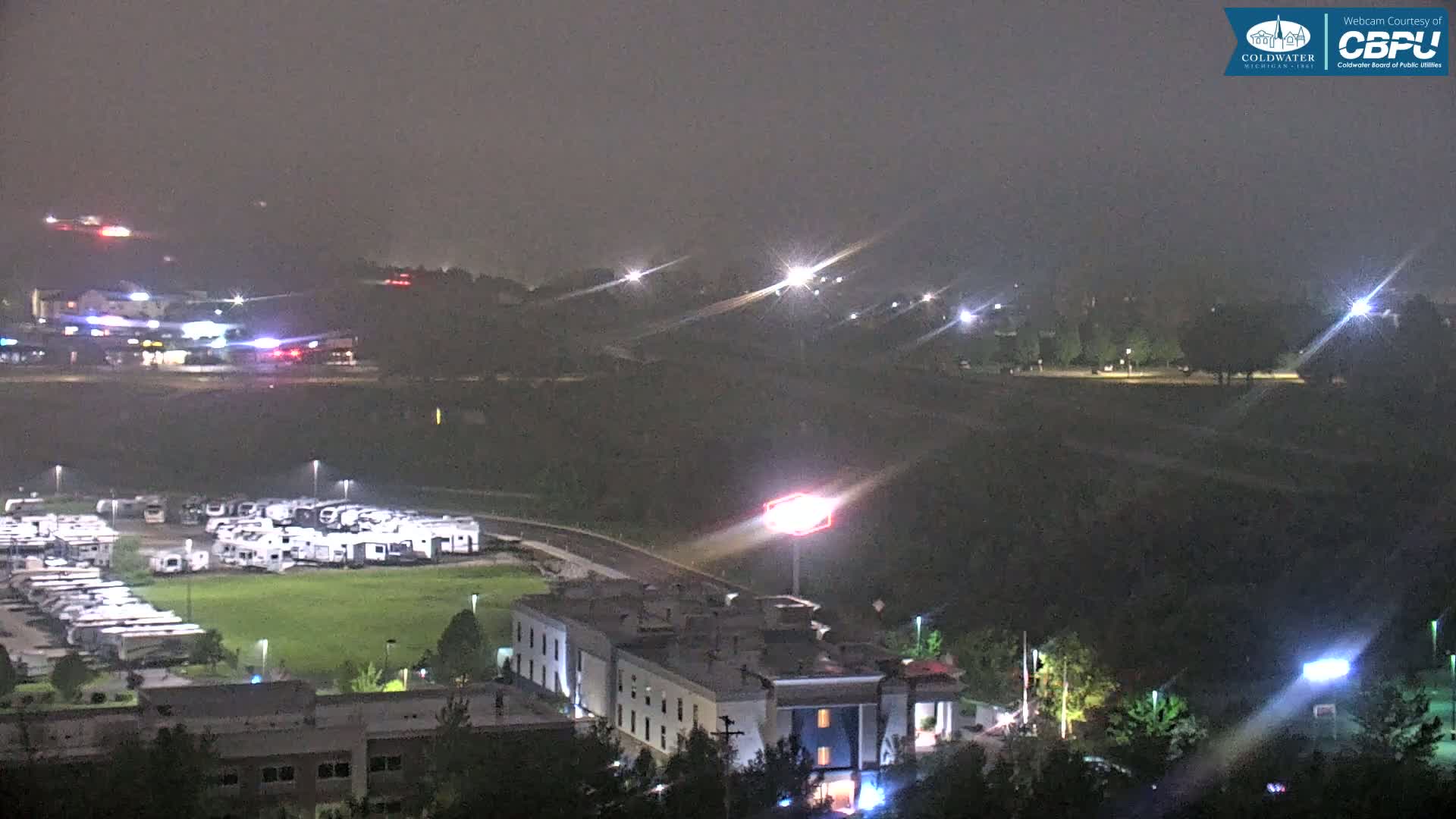 A nighttime view of a motel, a large RV park, and surrounding dimly lit areas under hazy conditions.