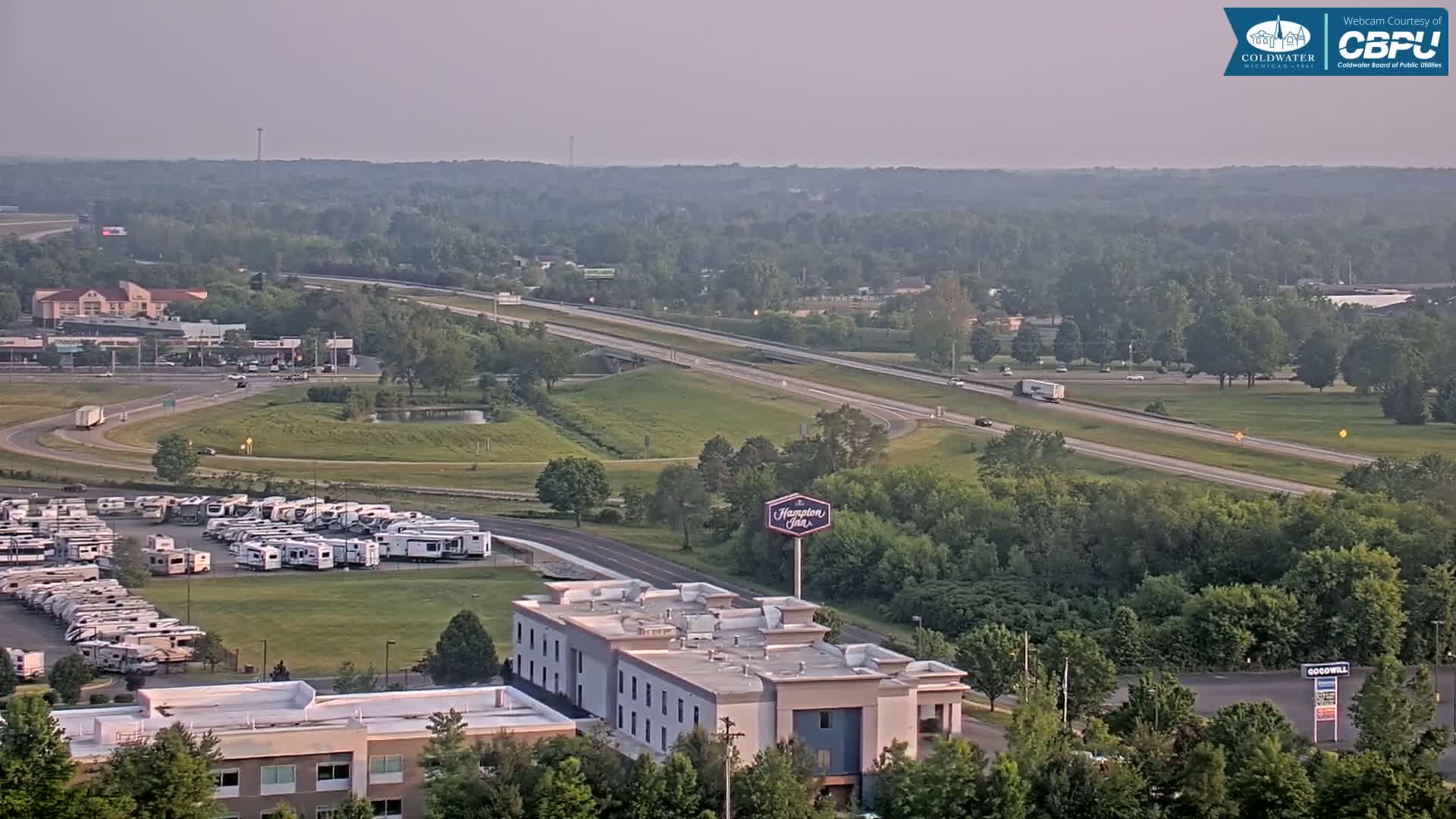 A hazy, summer day reveals a highway scene with a Hampton Inn, a large RV park, and surrounding green landscape.