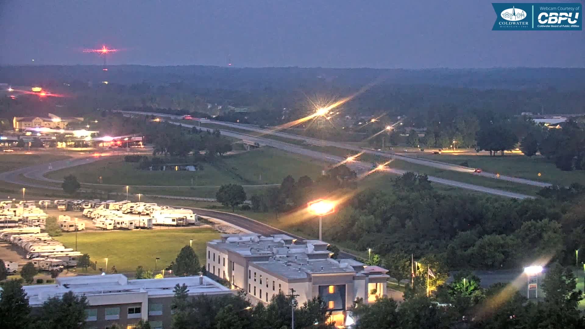 A twilight view of a highway and surrounding area, including a large RV park and a hotel, under a clear, dark sky.