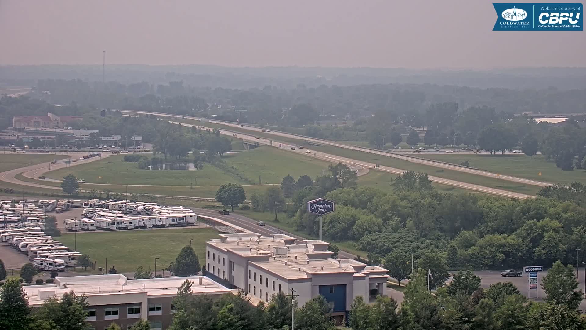 A hazy view shows a highway with moderate traffic, a large RV park, a Hampton Inn, and surrounding green areas.