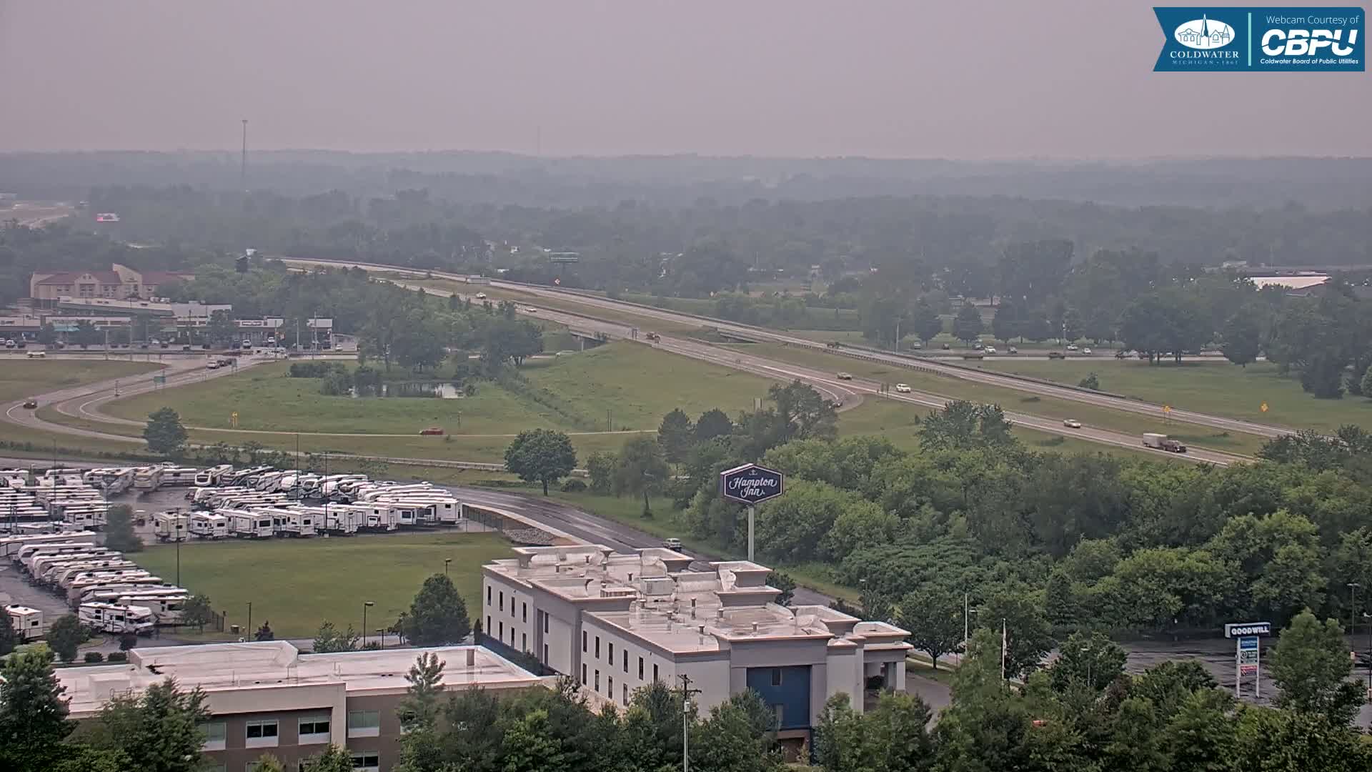 A hazy view of a highway, a large RV lot, a Hampton Inn, and surrounding green trees.