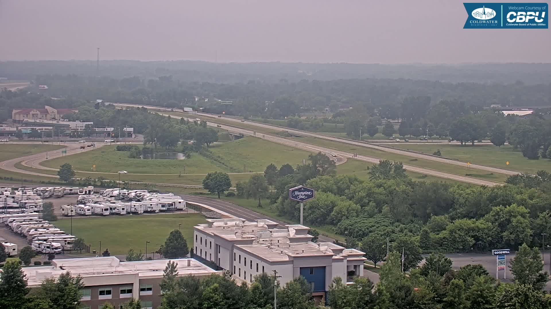 A hazy view of a highway, a large RV park, a Hampton Inn, and surrounding green landscape.