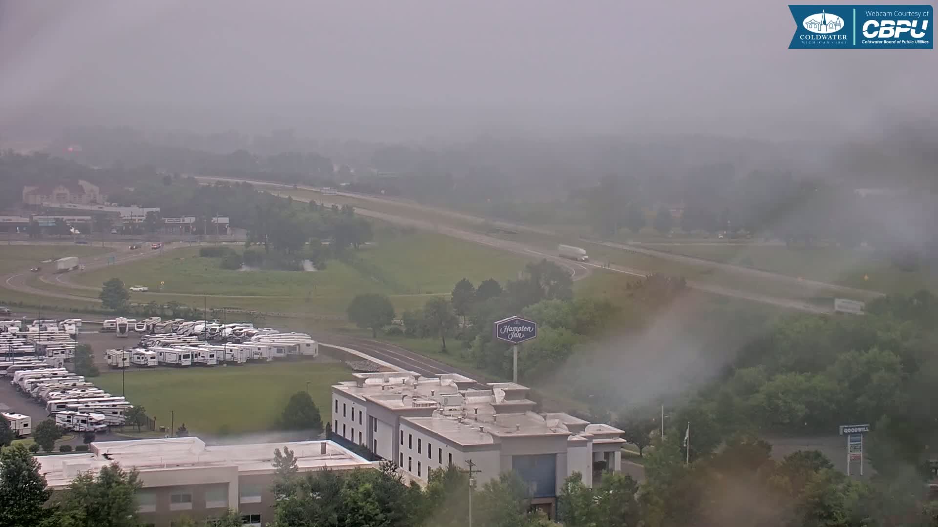 A hazy, overcast day reveals a highway, a large RV park, a Hampton Inn, and surrounding greenery.