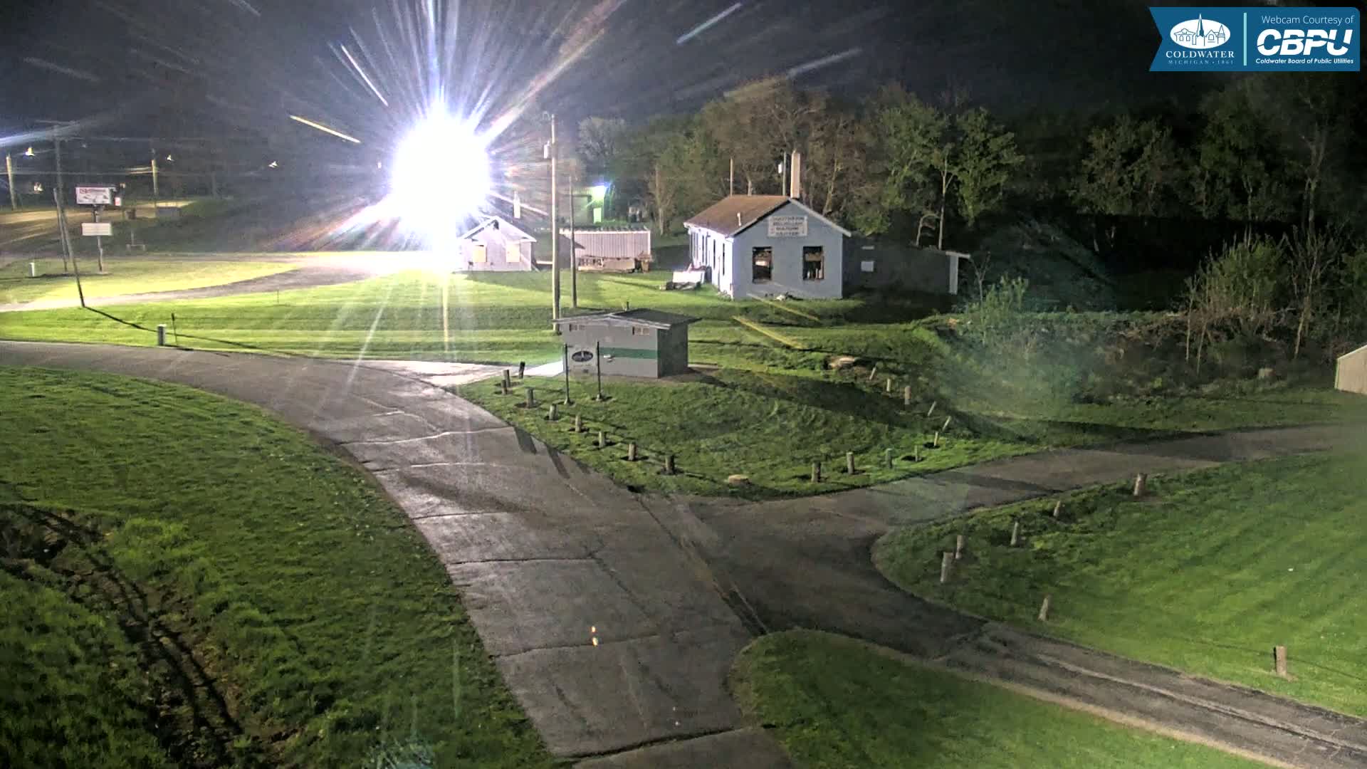 At night, a paved area with grassy areas and several small buildings is brightly lit, revealing a mostly clear sky.