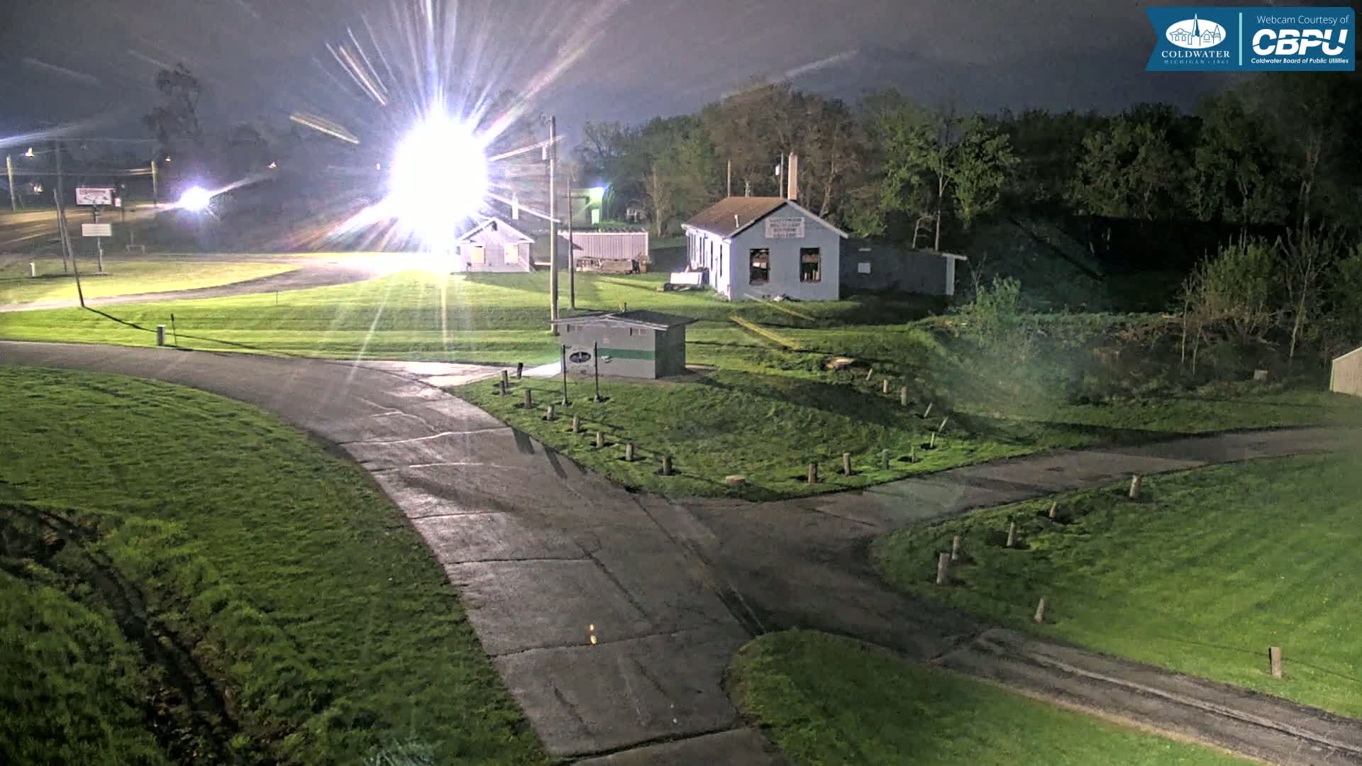 A nighttime view of a grassy area with roads and small buildings, illuminated by bright lights.