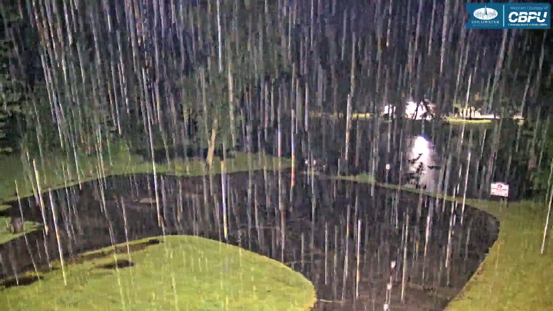A nighttime scene of heavy rain falling on a grassy area with a dark paved pathway curving through it.