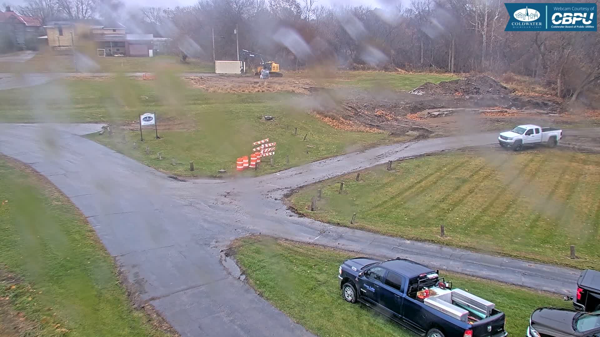 A dark asphalt boat launch area, bordered by grass and trees, sits next to a calm body of water under a night sky.