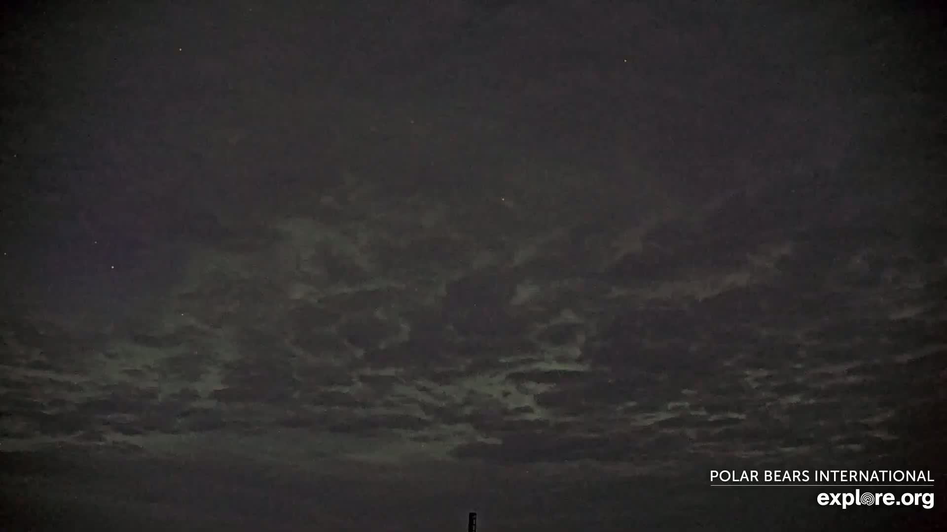A mostly cloudy night sky shows hints of green aurora borealis.