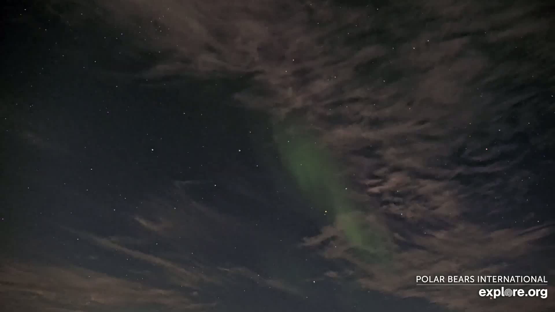 A nighttime sky shows a faint green aurora borealis through a layer of dark clouds and scattered stars.