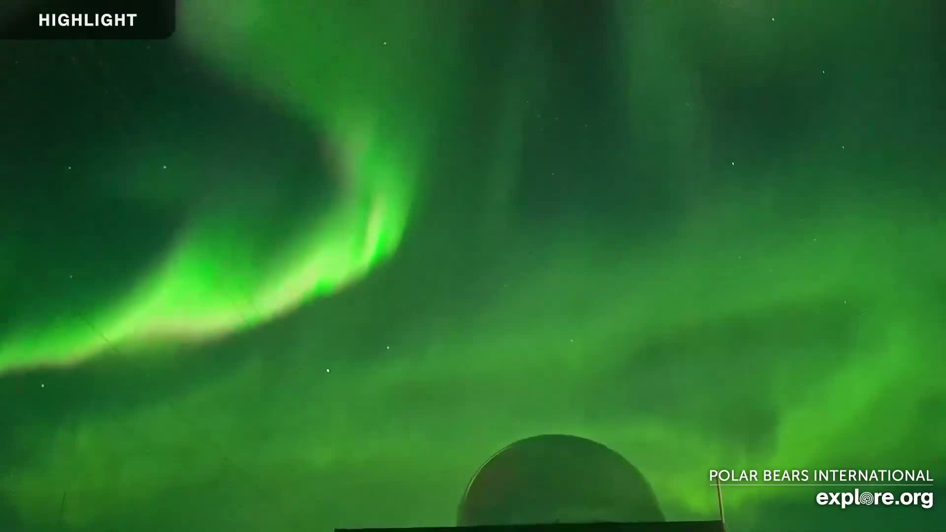 A vibrant green aurora borealis illuminates the night sky above a dark, dome-shaped structure.