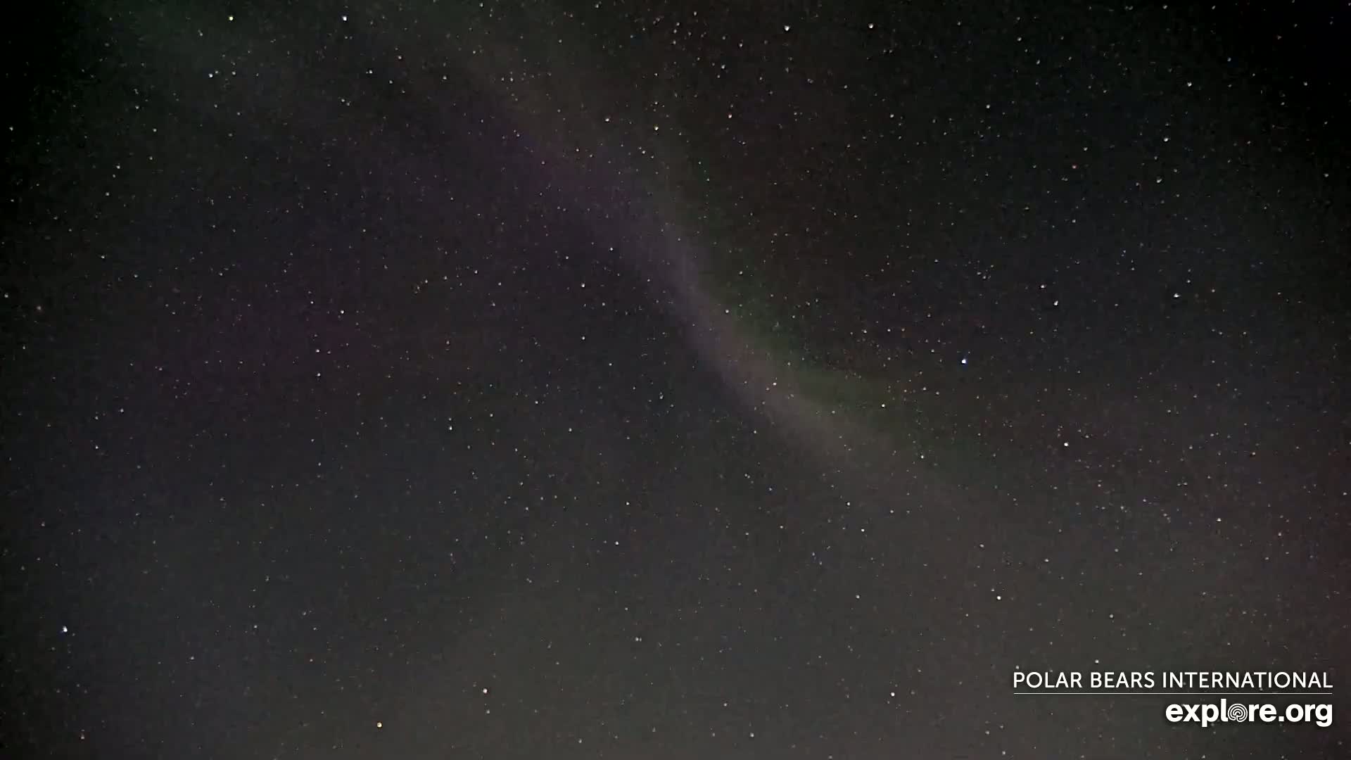 A nighttime sky shows a faint aurora borealis among numerous stars.